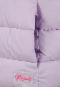 Lila kviltad tyg med en liten transparent glittrig patch som visar det rosa kursiva varumärket "Minoti".