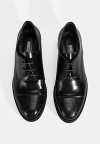 Chaussures habillées en cuir noir avec une finition brillante, présentant des détails perforés sur le bout, les lacets et une forme arrondie.