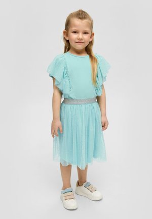 Ein hellblaues Kleid mit Rüschenshirts und einem glitzernden Bund. Der Rock besteht aus geschichtetem Tüll mit kleinen Sternmustern. Kombiniert mit weißen Sneakers.