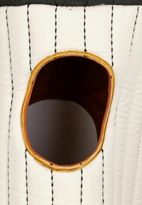 Oblačilo iz prešitega blaga, večinoma belo s črnimi šivi, z okroglim odprtinom obrobljenim z zlatimi šivi. Notranjost je rjava.