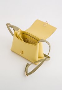 Sac à main en cuir jaune avec un accent doré, doté d'une bandoulière verte et d'un haut ouvert. L'intérieur comprend plusieurs compartiments et une poche zippée.