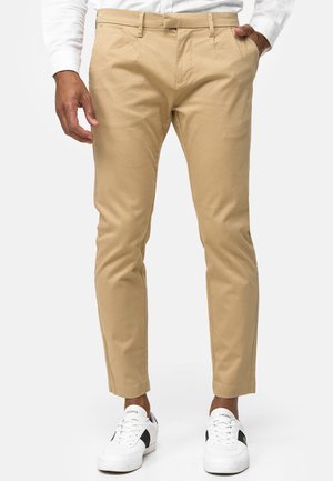 Chinos beige con un corte ajustado, que cuentan con bolsillos laterales y pasadores para cinturón, combinados con zapatillas blancas. Tela de algodón suave, diseño ajustado.