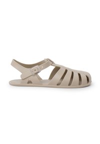Sandal de tiras beige hecho de plástico flexible, con un diseño de punta abierta, tirante al tobillo con hebilla y detalles recortados en los laterales.