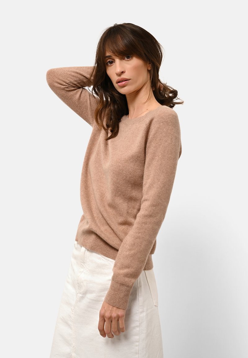 Beige Kaschmirpullover mit runder Ausschnitt, langen Ärmeln und gerippten Bündchen. Kombiniert mit einem weißen, hoch geschnittenen Rock.