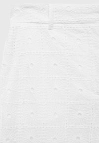Witte stof met textuur van bloemmotieven, voorzien van gestikte vierkanten en verhoogde cirkelvormige accenten. Glad afwerking, licht doorschijnend uiterlijk.