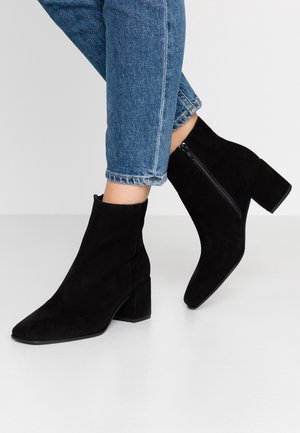 Schwarze Wildleder-Stiefeletten mit spitzem Zehenbereich und mittelhohem Blockabsatz. Verfügt über einen seitlichen Reißverschluss und eine glatte Textur. Tragen Sie sie mit verkürzten blauen Jeans.