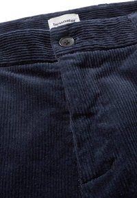 Marineblaue Cordhosen verfügen über eine gerippte Struktur, einen einzelnen Knopfverschluss und ein Etikett mit der Aufschrift "hessnatur" am Bund.