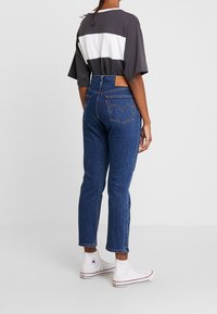 Jeans de tiro alto en azul con un diseño clásico de cinco bolsillos, denim texturizado y costuras en contraste, combinados con una camisa a rayas gris y blanca.