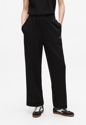 Zwarte sportbroek met een wijde pasvorm, gemaakt van zachte stof, met een elastische tailleband en verspreide strassteentjes rondom de zoom.