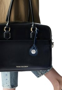 Borsa in pelle nera con finiture dorate e un ciondolo a forma di orologio blu attaccato. Presenta una superficie liscia e una forma rettangolare semplice.