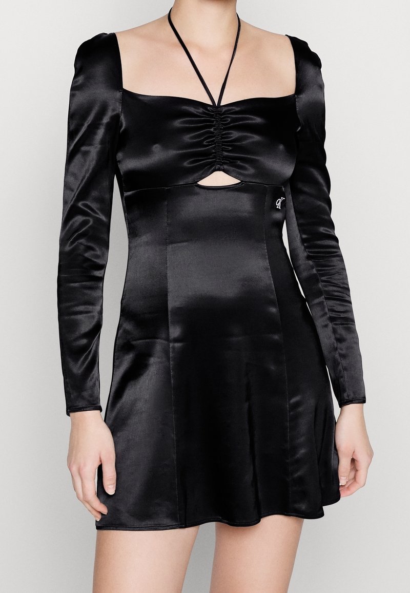 Černé saténové šaty s dlouhými rukávy, čtvercovým výstřihem, nařaseným detailem vpředu, výřezem na hrudi a přiléhavým trupem, který se rozšiřuje.