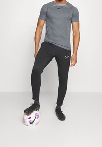 Grå sport-t-shirt kombinerad med svarta sweatpants. Outfitten har en liten vit Nike-logotyp och kompletteras med svarta fotbollsskor på en mönstrad boll.