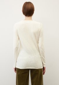 Langärmliges Creme-Baumwolloberteil mit Rundhalsausschnitt, glatter Textur und subtiler Melange-Optik, kombiniert mit olivgrünen Cordhosen.