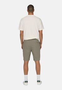 Tricou gri deschis, vedere din spate, asortat cu pantaloni scurți verzi măslinii. Pantalonii scurți au un buzunar pe spate și o croială lejeră, completată de șosete albe și pantofi sport.