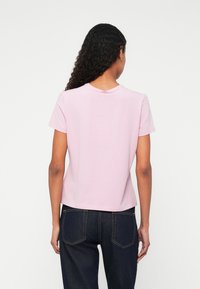 Tricou scurt din bumbac roz, cu decolteu rotund și mâneci scurte. Spatele are o textură netedă și un tiv ușor mai lung.