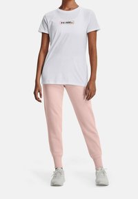 Vit t-shirt med kort ärm och en flerfärgad logotyp på bröstet, tillsammans med ljusrosa joggers och grå träningsskor. Slät textur.