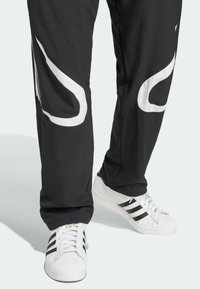 Svarta träningsbyxor med vita sidoremsor, kombinerade med vita sneakers med svarta ränder och en texturerad tåhätta.