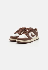 Brown and white Nike sneakers with a perforated toe box, round laces, and a textured sole. Features a prominent swoosh logo on the side.