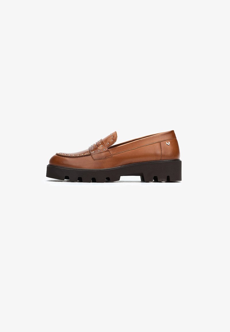 Mocasín de cuero marrón con detalles de tachuelas, que presenta una puntera redondeada y una suela gruesa negra. Textura suave y diseño minimalista.