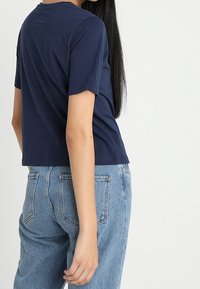 T-shirt blu navy a maniche corte con scollatura tonda e vestibilità corta, abbinato a jeans denim chiari a vita alta con tasche posteriori.