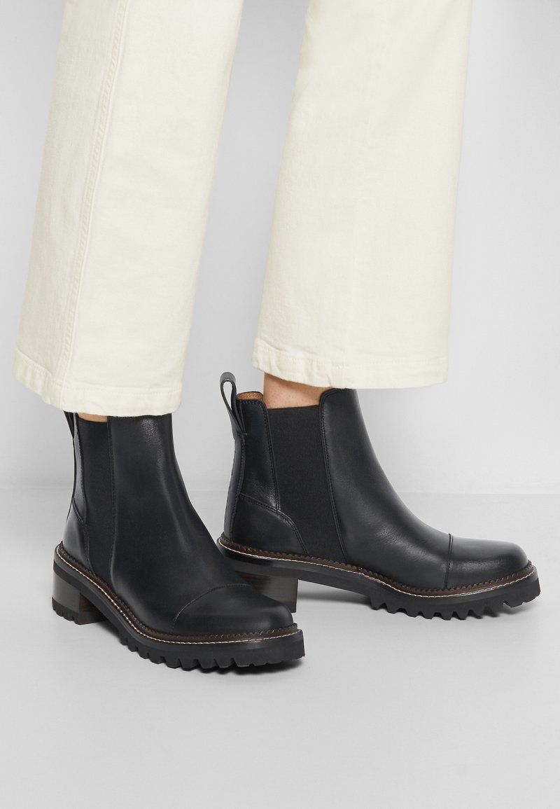 Bottines en cuir noir avec des panneaux latéraux élastiques, bout rond et semelle en caoutchouc noir texturé. Des coutures marron rehaussent les bords.