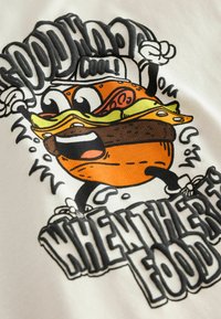 Grafikus póló, amely egy rajzfilmes hamburger mintáját ábrázolja narancssárga húspogácsával, sajttal és salátával. A felirat így szól: "JÓ HANGULAT" és "AMIKOR VAN ÉTEL."