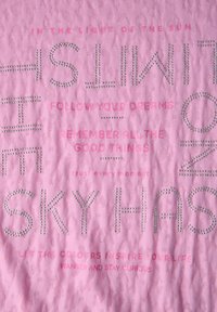Tela rosa con textura en relieve y tachuelas plateadas. El texto incluye frases motivacionales en diferentes tamaños y estilos.