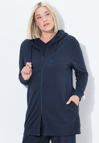 Giacca a vento blu navy con zip frontale, caratterizzata da una vestibilità comoda, tasche laterali e accenti blu chiaro a contrasto sui polsini e sulla zip.