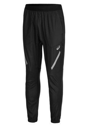 Mężczyzna noszący czarne spodnie sportowe z odblaskowymi detalami i kolorowe buty do biegania, stojący na białym tle.