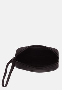 Funda negra con cremallera y textura suave, con una sola correa para la muñeca y un interior sin forro. Abierta para revelar un amplio espacio de almacenamiento.