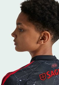 Maglia sportiva nera da gioventù con accenti rossi, un motivo a costellazioni e dettagli del logo sulla schiena e sulla spalla. Maniche corte e collo rotondo.