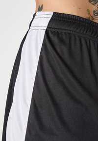 Zwarte sportshorts gemaakt van een gladde stof, met een contrasterende witte zijkant, een elastische tailleband en een minimalistisch ontwerp.