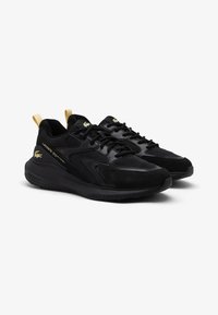 Czarne sportowe sneakersy z połączeniem gładkich i teksturowanych materiałów, z żółtymi akcentami na piętach i subtelnym logo w kolorze złotym.