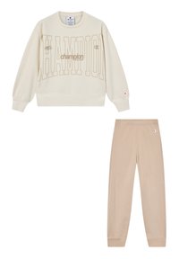 Sudadera de Champion crema con gran texto de logo y pantalones de chándal beige, ambos con pequeños logos bordados de Champion en las mangas y las caderas.