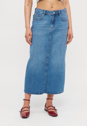 Mellem-lang blå denim nederdel med søm foran, båret med røde patentlæder Mary Jane sko på en person med en lille tatovering på armen.