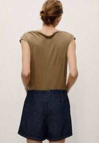 Brown, short-sleeve shirt paired with dark blue denim shorts. The fabric appears soft, with a relaxed fit and no visible patterns or hardware.