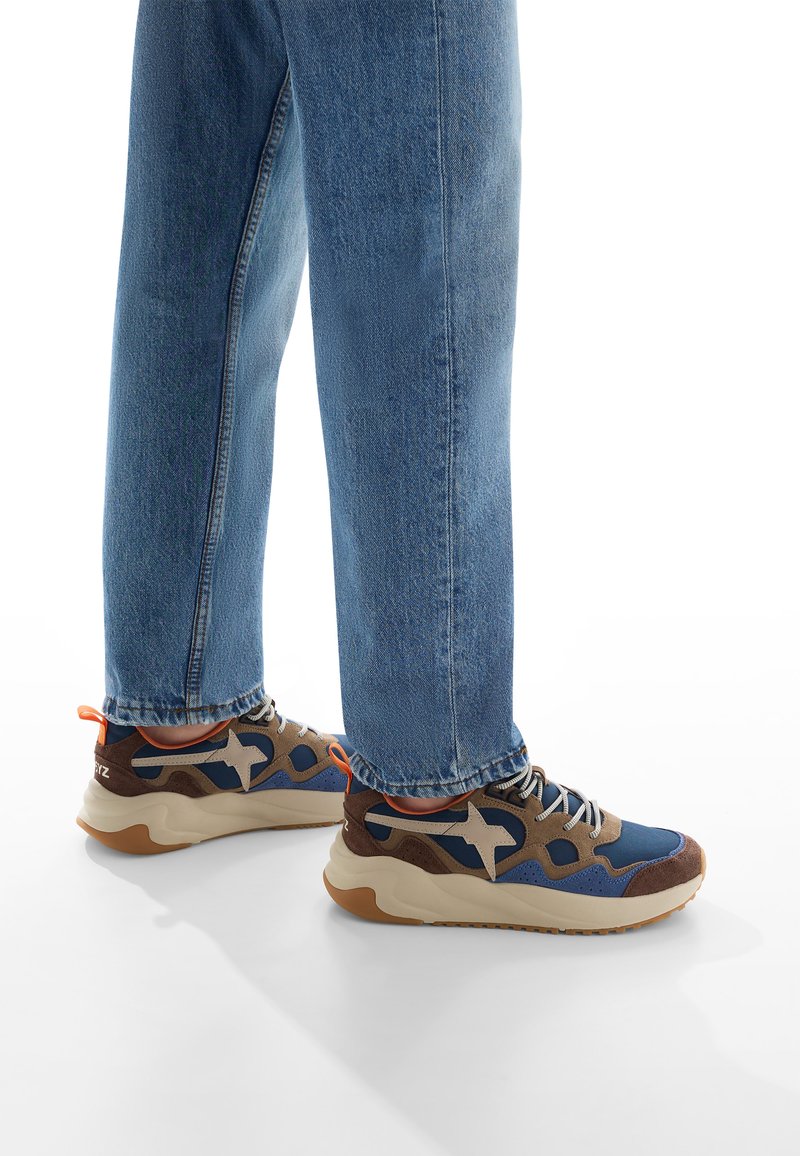 Tenisky se směsicí modré látky, hnědé semišové detaily a světle béžovými podrážkami. Dokončeno šedými tkaničkami a oranžovým poutkem na patě.