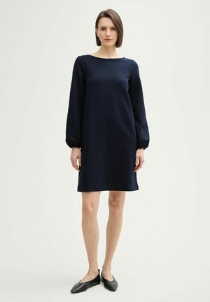 Abito blu navy, a maniche lunghe, con scollatura tonda e polsini elasticizzati, caratterizzato da una silhouette dritta e una texture morbida. Indossato con ballerine nere.