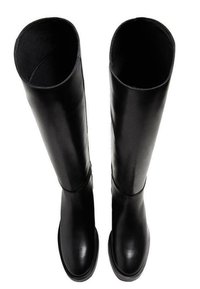 Bottes montantes en cuir noir à texture lisse, bout arrondi et tige large et ouverte. Semelle plate avec des accents minimaux.