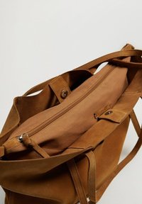 Brązowa torba z zamszu z długimi uchwytami i wewnętrzną kieszenią na zamek błyskawiczny, przedstawiona z widokiem od góry, z zapięciem na zatrzask.