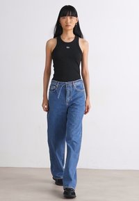 Schwarzes ärmelloses Oberteil und weite blaue Jeans. Glattes Baumwollmaterial mit entspannter Passform. Schwarze Sneakers mit strukturiertem Boden. Minimalistisches Design.
