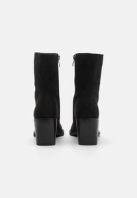 Mustat mokkanahkast ankle boots, joissa on sylinterimäinen korko, takana vetoketjusulku ja sileä, matta pinta. Yksinkertainen muotoilu ilman koristeluja.