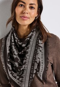 Svart och grå mönstrad scarf med fransade kanter och textdetaljer, draperad runt halsen, tillverkad av ett mjukt, texturerat material.