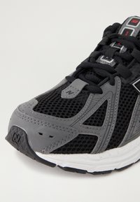 Baskets de sport noires avec une tige en mesh respirant agrémentée d'accents gris, un renfort au niveau des orteils et une semelle en caoutchouc texturé pour une meilleure adhérence.