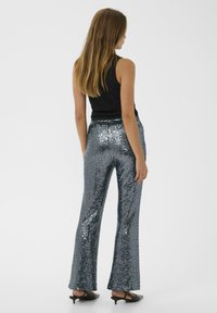Flared sequin pants in a shiny silver-grey color, featuring a smooth texture and elastic waistband. Worn with a black sleeveless top.