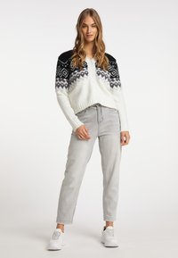 Cardigan lavorato a maglia con corpo bianco, spalle nere decorate e dettagli grigi. Abbinato a jeans grigi e sneaker bianche.