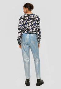 Zwarte blouse met een bloemenpatroon in het wit, roze en blauw. Lichtblauwe metallic hoge broek. Zwarte laarzen met dikke zolen.