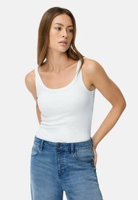 Weißes ärmelloses Tanktop mit rundem Ausschnitt, kombiniert mit hellblauen Jeans. Der Stoff wirkt glatt und enganliegend.