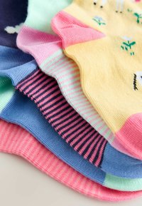 Stapeltje van vijf kleurrijke enkelsokken met verschillende strepen en een geel paar met kleine bloemmotieven en roze tenen.