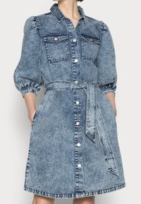 Denim-mekko nappilistalla, puffihäillä, rintataskuilla ja yhteensopivalla vyöllä, joka on solmittu vyötärölle.